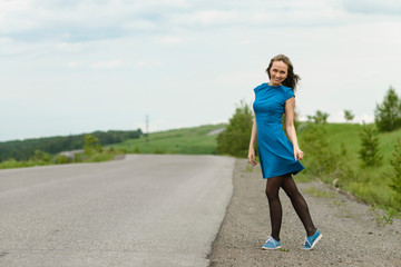 Beautiful woman in a blue dress posing on a road over landscape