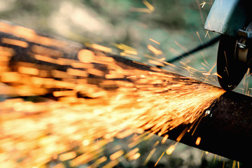 Sawing a metal pipe with a circular saw with sparks flying toward the side