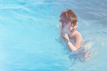 Fototapeta na wymiar Happy little boy is swimming in the pool