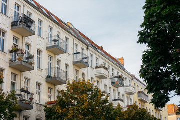 white apartment house with steel balcony and green tree on the right side