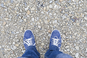 Texture of stones with sharp edges and legs in jeans and blue sneakers