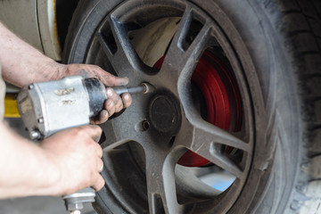 Mechanic unscrews automobile wheel with pneumatic tool
