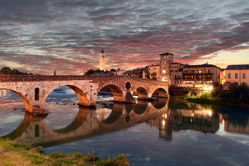 Fototapeta premium Roman empire ancient bridge Ponte Pietra over the river Adige in Verona, Italy during sunset with illuminated old town