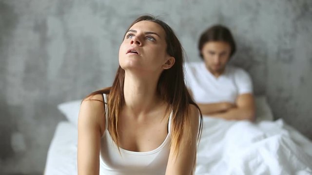 Unhappy young couple sitting apart on bed in bedroom after conflict, having problems misunderstandings in difficult relationships, thoughtful worried frustrated woman feeling troubled offended