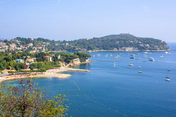 Fototapeta premium Beautiful daylight view from top of mountains to luxury resort villefranche sur mer and bay on french riviera at mediterranean sea Cote d'Azur in France, beach with boats cruising on water.