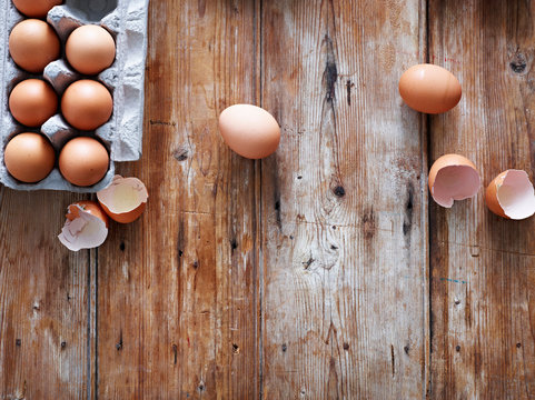Eggs in egg box and broken shells on wooden surface, overhead view