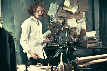 Writer at work. Handsome young writer standing near the table and making up something in his mind