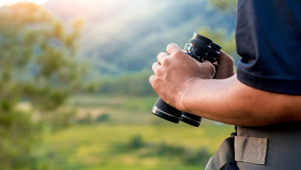 Hiker man holding binoculars on the mountains with a backpack