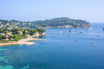 Fototapeta premium Beautiful daylight view from top of mountains to luxury resort villefranche sur mer and bay on french riviera at mediterranean sea Cote d'Azur in France, beach with boats cruising on water.