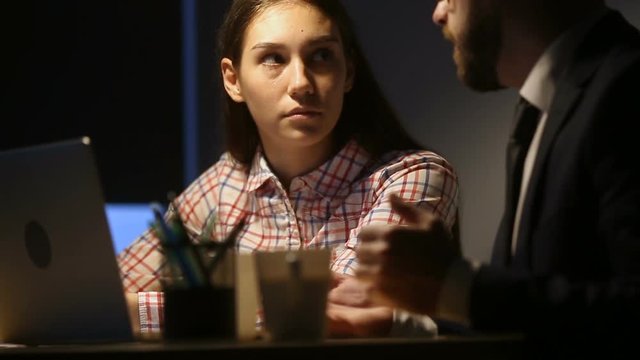 Female trainee listening to mentor coach teaching young woman in office with laptop, business leader talks to intern sitting under lamp light, coworkers working on project late talking sharing ideas