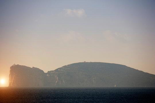 Hazy coastal view with cliff top lighthouse, Capo Caccia, Sardinia, Italy