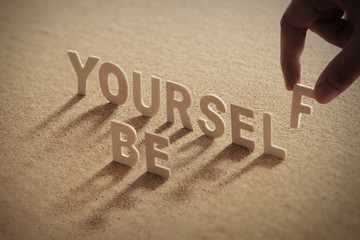 BE YOURSELF wood word on compressed or corkboard with human's finger at F letter.
