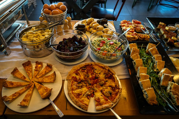 Greek breakfast buffet table full with varieties of pizza, pies, pasta, beetroot, couscous salads, boiled eggs, local dishes, etc.