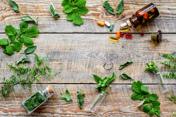 Healing herbs. Fresh leaves, bottles and pills on wooden background top view copyspace