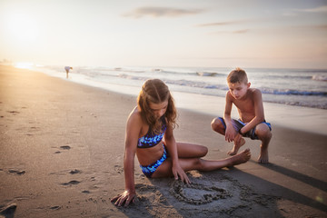 Girl drawing heart in sand on beach