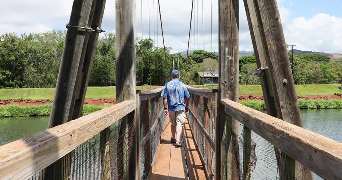 Hanapepe swinging bridge man walks away Kauai Hawaii. Wooden bridge built in early 1900 to allow people to cross the river from the residential area to the business street area. Unique foot path.