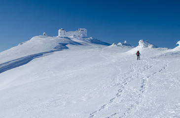 Winter picture of a hiker walking towards the abandoned observatory atop the mountain Pip Ivan in Ukrainian Carpathians. It goes through the process of reconstruction now