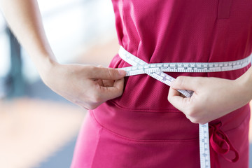 Close up Sport woman measuring her waist by using waistline, comparing her waist size before and after workout for firming body - Healthcare concept
