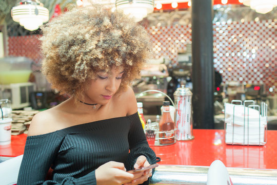 Young woman sitting in diner, looking at smartphone