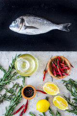 Dorado ready to cook with spices rosemary, pepper, chili, lemon on black and grey background top view