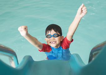 Asian happy kid playing slider in swimming pool