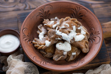Clay plate with rye dumplings or vareniki stuffed with sauerkraut and topped with sour cream, selective focus, closeup