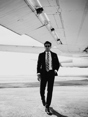 Serious handsome young man in the west and suit walk near plane on the airfield