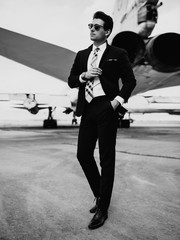 Serious handsome young man in the west and suit walk near plane on the airfield