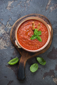 Bowl of gazpacho tomato soup on a rustic wooden serving board, flat-lay on a brown stone background
