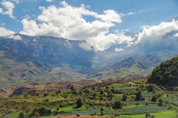 Fototapeta premium Krajobraz gór Kaukazu w lecie. Malowniczy widok na dolinę, pola uprawne i col na grzbiecie górskim. Natura i podróże. Rosja, Dagestan