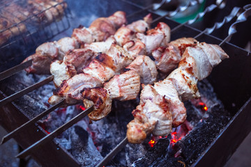 Grilled kebab cooking on metal skewers (grill). Roasted meat cooked at barbecue with smoke. Close up BBQ fresh pork meat chop slices. Traditional eastern dish, shish kebab.