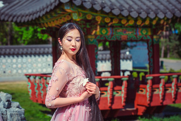 Girl in pink dress holding a flower in the hand, on a background of a traditional Japanese temple, in the park