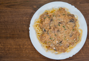 Sliced fried chicken meat and mushroom in a creamy sauce with spaghetti pasta in a plate  on a wooden background. with copy space. top view