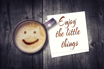 Enjoy the little things inspirational note on paper card with coffee cup on wooden background