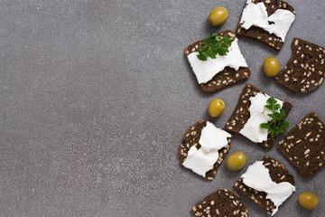 Black toasted bread with cheese and grains on a gray surface. View from above.