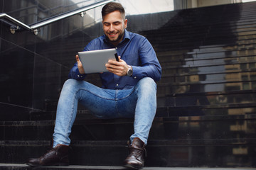 Fototapeta na wymiar Young handsome man sitting on stairs and using digital tablet outdoors