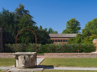 Historic well in the garden of the Pomposa Abbey Monastery with the “Palazzo della Ragione” building in the background. Codigoro, Ferrara, Italy
