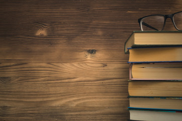 Education. Stacked Books and glasses on wooden wall background with copy space.