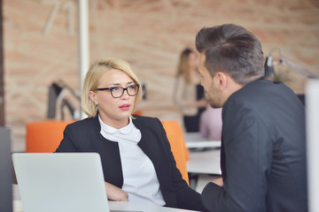 Beautiful young business partners are using a laptop, discussing documents and smiling while working in office.