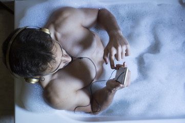naked guy in bathroom with smartphone and headphones
