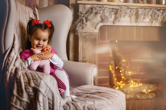 A very excited young girl sits backwards in a chair on Christmas morning. She is eager to get through breakfast and open gifts. She is wearing a Santa dress and a silver bow on her head.