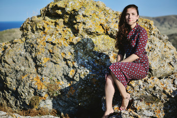 Naklejka premium Young beautiful girl sits on a stone, straight calm look. Emotions: waiting, willingness, patience