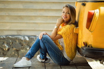 Happy smiling girl is wearing yellow sweater near old retro bus, autumn concept