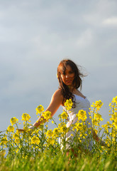 Naklejka na ściany i meble A beautiful young girl strolls happily through a rape seed field on a summer evening. Filled with happiness and joy she admires the colorful yellow flowers as the sun passes through. 