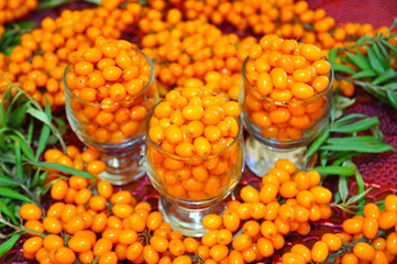 3 glasses filled with ripe sea-buckthorn berries on the background of sea-buckthorn bunches