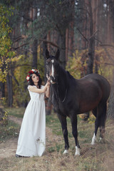 Fototapeta premium autumn portrait of romantic woman with flowers in her hair near with a horse