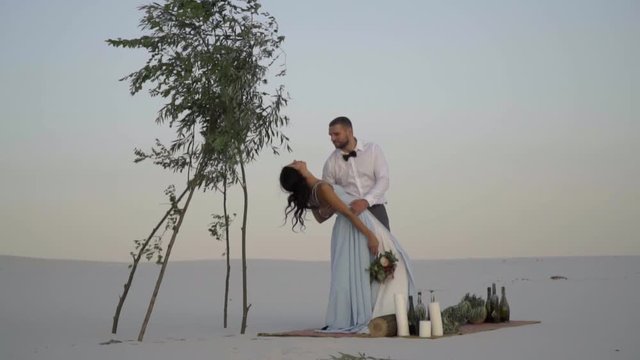 A woman in the arms of a man arches back, he kisses her neck, romance in the desert. Slow motion