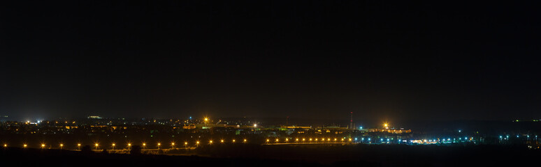 Fototapeta premium The bright lights of the city streets in the background of the night sky. Panoramic view of residential areas.