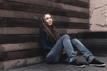 beautiful young girl with dreadlocks posing on the street sitting near a wooden wall