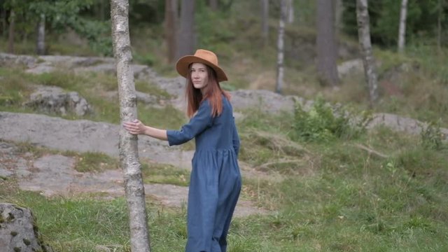 Young woman in brown hat and blue dress shirt with long hair walking in the pine tree forest